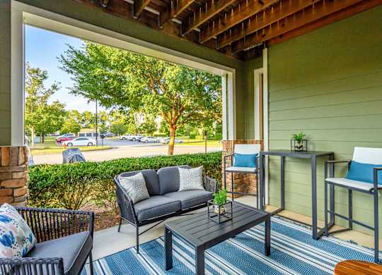 A patio with a black sofa, a black chair, and a small table with a plant on it.