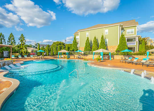 A large swimming pool with a fountain in the middle surrounded by a wooden deck and lounge chairs.