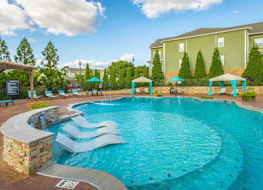 A large swimming pool with a stone wall and a bench.