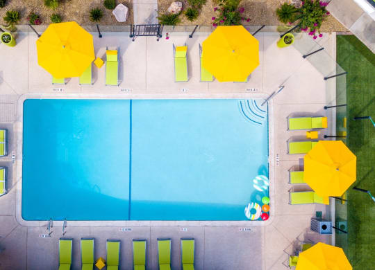 Aerial view of Fusion Las Vegas apartments 89119 community pool surrounded by lime green lounge chairs and cabanas with bright yellow umbrellas.
