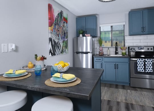 Fusion Las Vegas apartment kitchen with blue cabinets with black pulls, electric stove, and stainless steel refrigerator.
