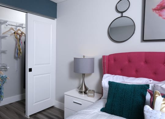 Fusion Las Vegas studio apts in Las Vegas NV. Apartment closet white doors and built in wire shelving next to bed with hot pink headboard and teal crochet pillow.