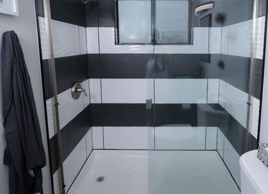 Fusion Las Vegas apartment shower with modern black and white tiles, black grout, sliding glass doors, and chrome plated fixtures.