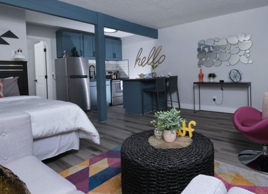 Fusion Las Vegas studio apartment with colorful geometric rug, fuchsia living room chair, and potted greenery on wicker coffee table.