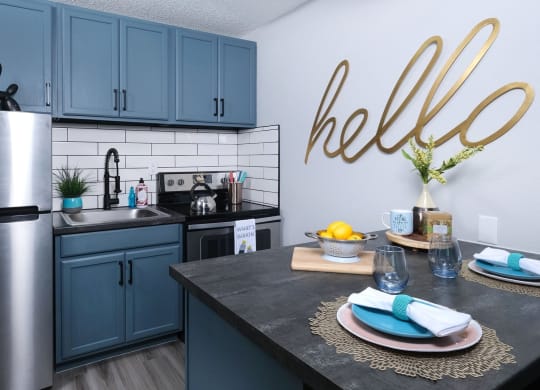 Fusion Las Vegas apartment kitchen with stainless steel electric stove and basin sink, and a large gold sign that reads "hello" in cursive.