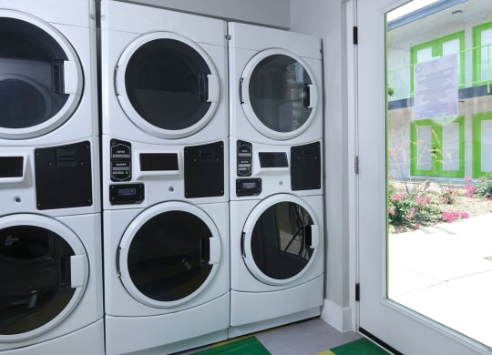 Fusion Las Vegas apartments on site laundry room with six front load washer dryer units next to glass door to courtyard.