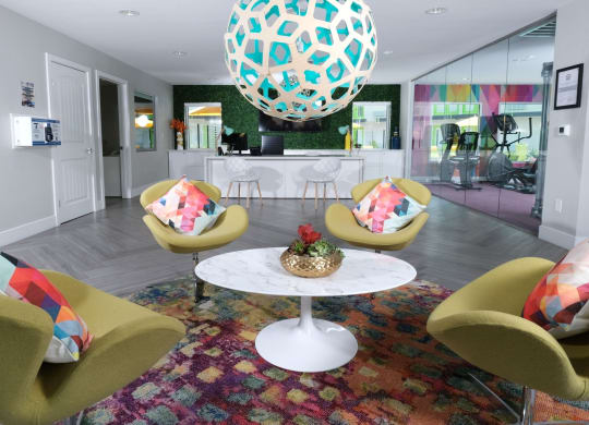 Fusion Las Vegas apartments lobby sitting area with four green chairs and geometric throw pillows around a round coffee table and modern light fixture.