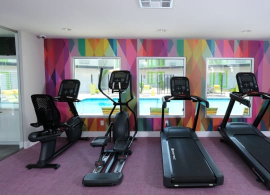 Cardio machines looking out three large windows in a colorful wall in the fitness center at Fusion Las Vegas Apartments, 89119.