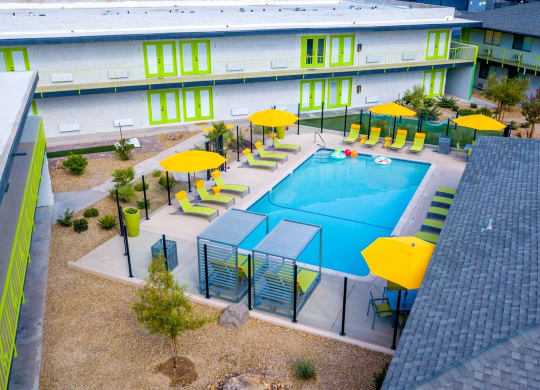 Aerial view of Fusion Las Vegas Apartments with pool with tall clear fence panels with black fence posts and Fusion Los Vegas apartment buildings with lime green doors.