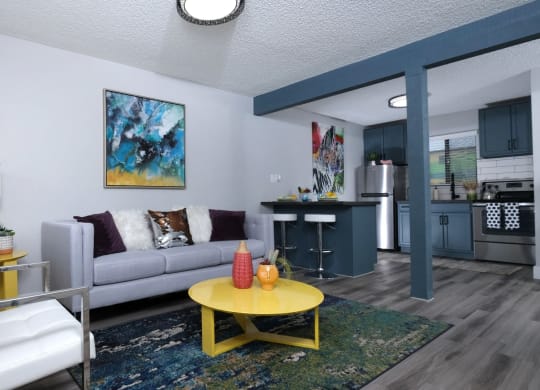 Fusion Las Vegas apartments 89119 open concept living area with modern blue and green, yellow coffee and side table, and view to kitchen.