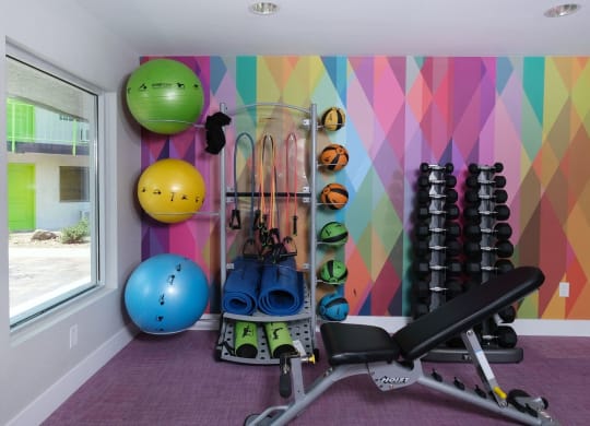 Fusion Las Vegas Apartments with fitness center with weight training equipment and body weight equipment stored against a colorful geometric wall.