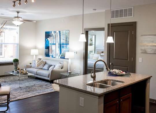 The living room in this updated modern interior at Austin Park Apartments in Miamisburg, Ohio showcases hardwood flooring, granite-style countertops, and a kitchen island, welcoming pets.