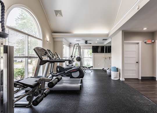 A fitness center equipped with a selection of workout equipment and large windows.