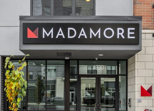 Front entrance of Madamore Apartments with a walkway and lush greenery.