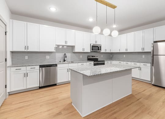 This modern kitchen is equipped with a central island providing workspace and stainless steel appliances, including a range and refrigerator.