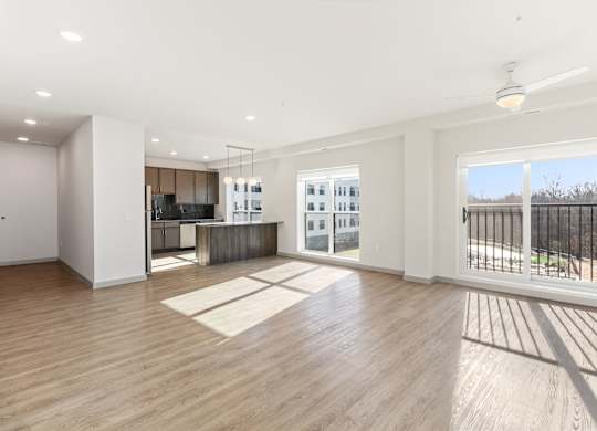 A spacious room with warm wooden flooring and a large window offering a view of a wooden fence.