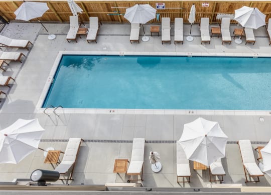 Aerial view of a swimming pool at Madamore with white chairs and umbrellas surrounded by a wooden fence.
