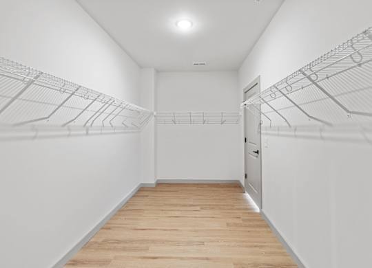 A well-lit long hallway closet with a plain white wall extends to a closed door at the far end.