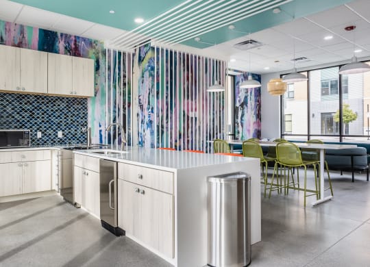 A lounge with a kitchen with stainless steel appliances, a light wood cabinets, next to a table and chairs.