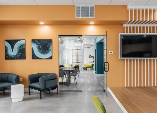 A lounge with two blue chairs, a TV, and a door leading to a seating area.