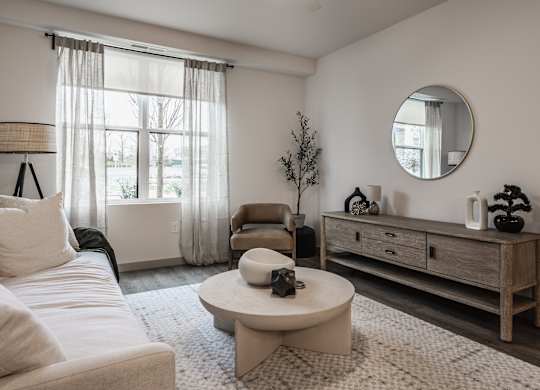 The living room offers a white sofa, a round accent table, and a closed wooden storage cabinet.