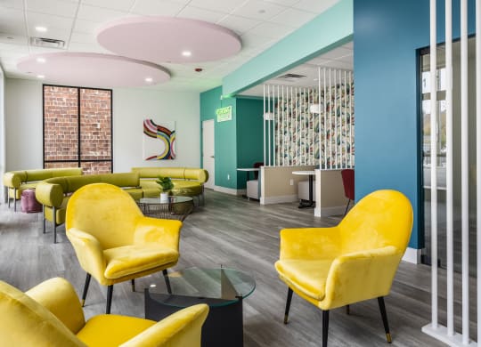 A co-working lounge with a table surrounded by three yellow chairs on hardwood-style flooring at Madamore.
