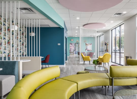 A green couch on hardwood-style floorings, next to tables and chairs in a co-working lounge.