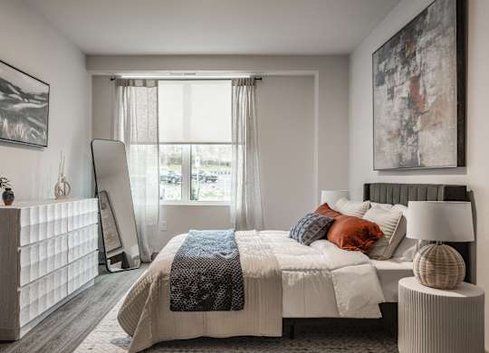The bedroom includes a substantial bed with linens and a framed painting displayed on the wall above it.