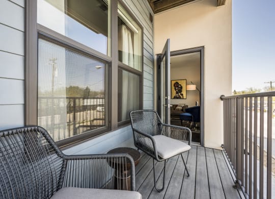 An apartment balcony with two chairs and a table in between, and a door leading to inside.