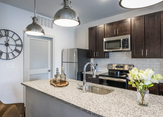 A kitchen with dark cabinets, an island, and stainless steel appliances at Madamore Apartments.