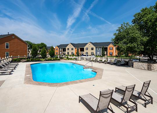 A swimming pool surrounded by lounge chairs and buildings in the background.