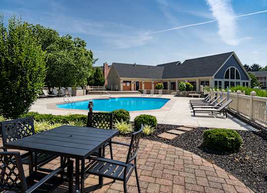 A black table and chairs are set up outside in front of a house with a pool.