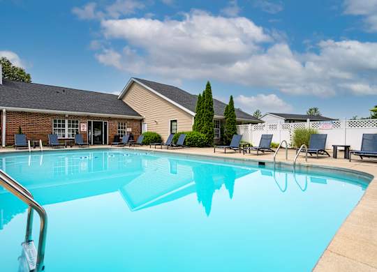 A large swimming pool in front of a building with a blue sky and clouds in the background.
