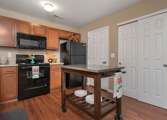 A kitchen with a black fridge and oven, wooden cabinets, and a wooden island with a towel hanging on it.