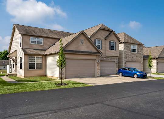 A blue car is parked in front of a house with a tree.
