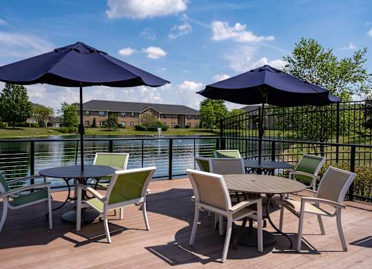 A table with chairs and umbrellas on a deck overlooking a lake.