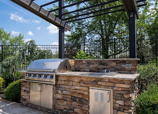A stone outdoor kitchen with a grill and a pergola.