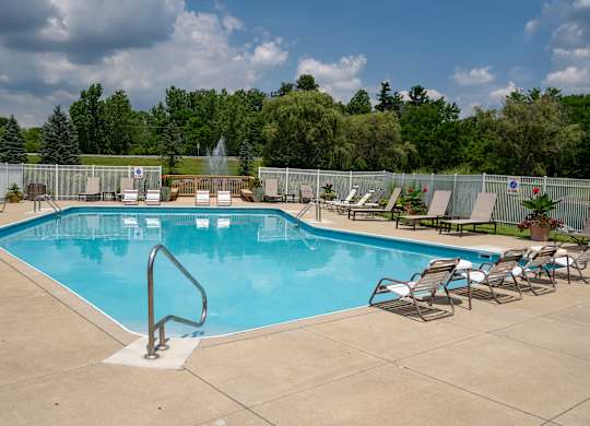A large outdoor swimming pool surrounded by a fence and lounge chairs.