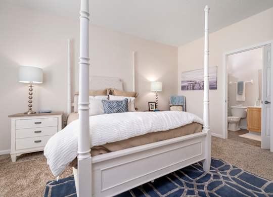 A white four poster bed with a white bedspread and pillow.