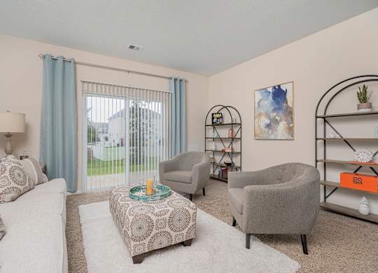 A living room with a white couch, grey armchair, and a patterned ottoman.
