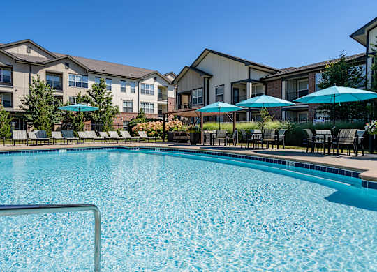 A swimming pool surrounded by apartment buildings and lounge chairs.