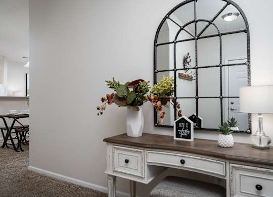 A white desk with a mirror and a vase of flowers.