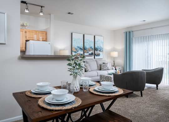 A dining table set with plates and glasses is in the foreground of a well-lit dining room.