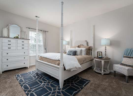 A bedroom with a white bed, a white dresser, and a white chair.