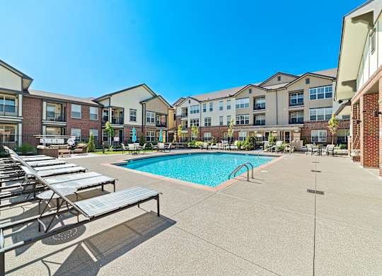 A resort-style swimming pool with a sundeck, lounge chairs, and well-kept landscaping.