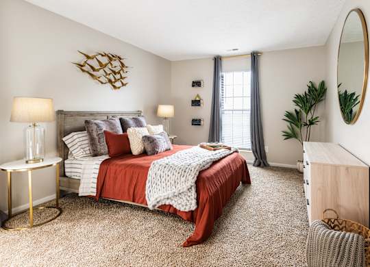 A bedroom at Fairway Lakes with a queen-sized bed, carpeted flooring, stylish decor, and a window.
