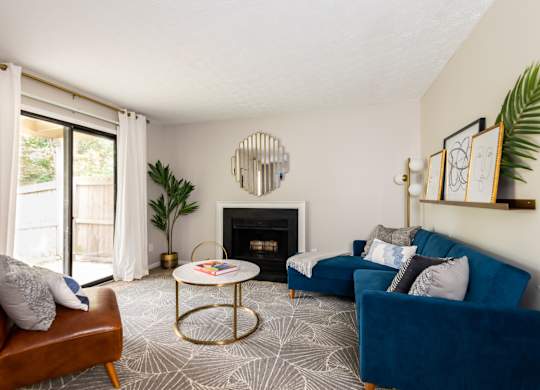 A living room featuring a blue couch, a fireplace, stylish decor, and a sliding glass door.