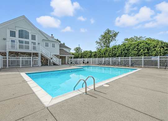 A swimming pool in front of a house with a deck.