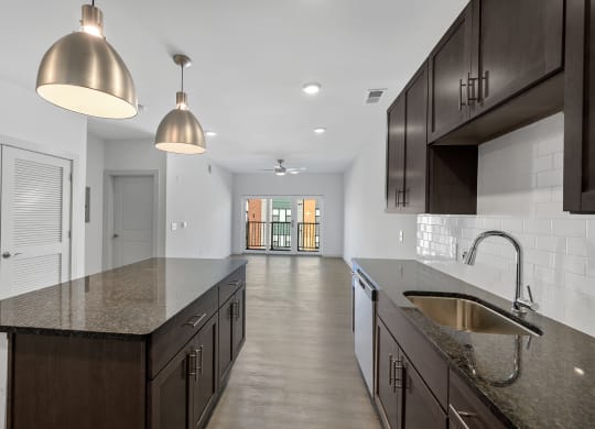 Madamore kitchen with dark wood cabinets and an island, next to a living room with a sliding glass door.