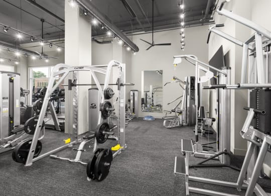 A fitness center at Madamore Apartments with workout machines, ceiling fans, and lights.